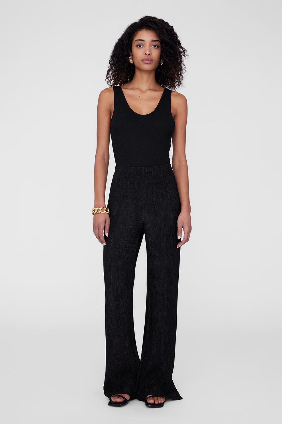 Black wide-leg pants with a textured finish, styled with a fitted black tank top and black sandals.