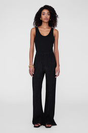 Black wide-leg pants with a textured finish, styled with a fitted black tank top and black sandals.