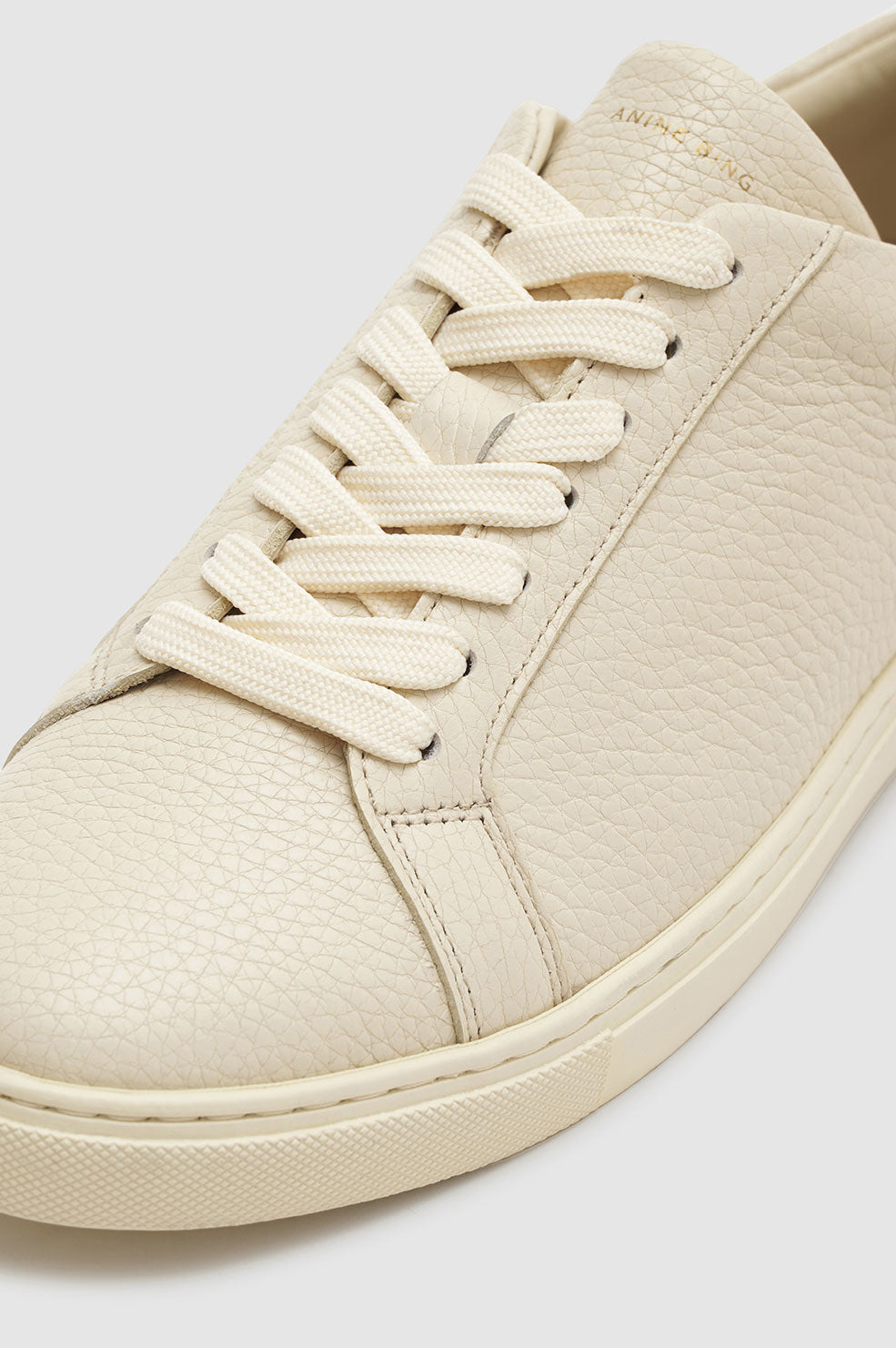 Light beige sneaker with a pebbled texture and cream laces, featuring a rounded toe and minimalistic design.