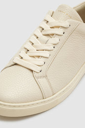 Light beige sneaker with a pebbled texture and cream laces, featuring a rounded toe and minimalistic design.