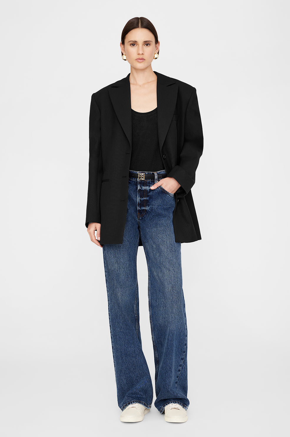 Model wearing a black oversized blazer, black tank top, and wide-leg blue jeans with sand pebbled sneakers.