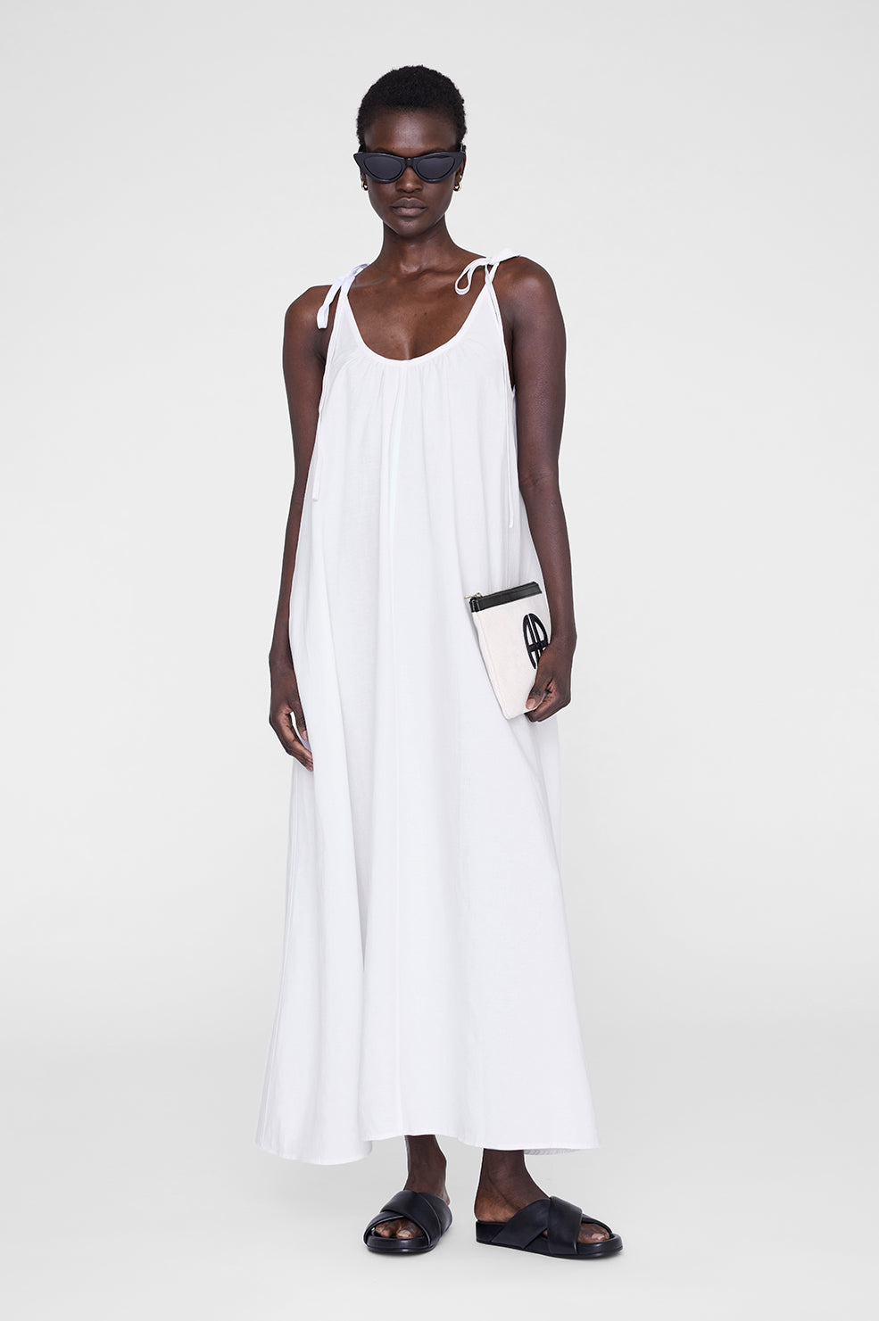 White maxi dress with adjustable straps, paired with black sunglasses and a small clutch bag.