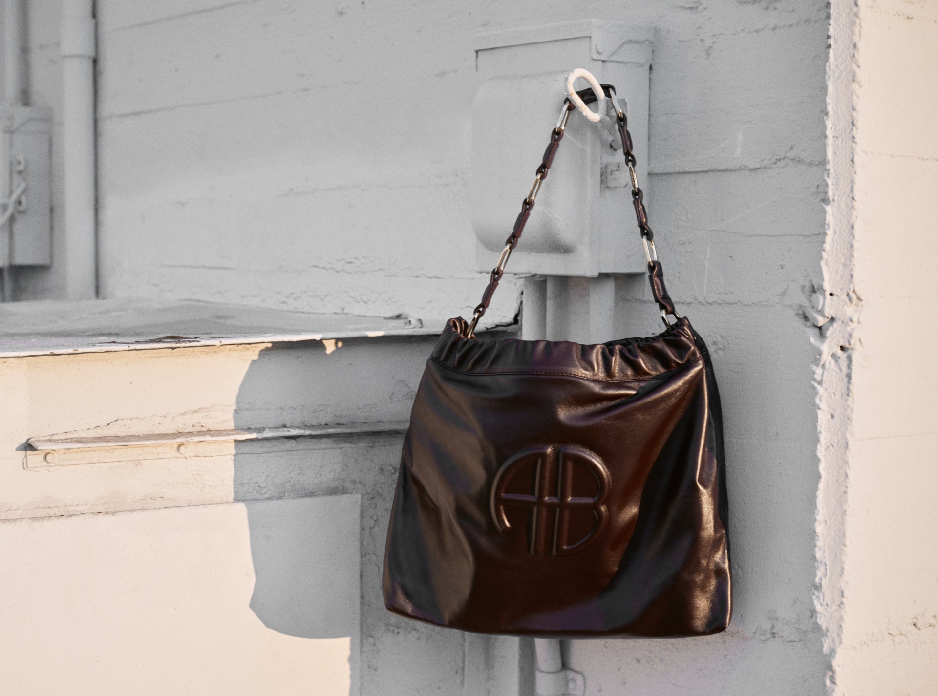 Shiny brown handbag with a logo attached to a light gray wall.