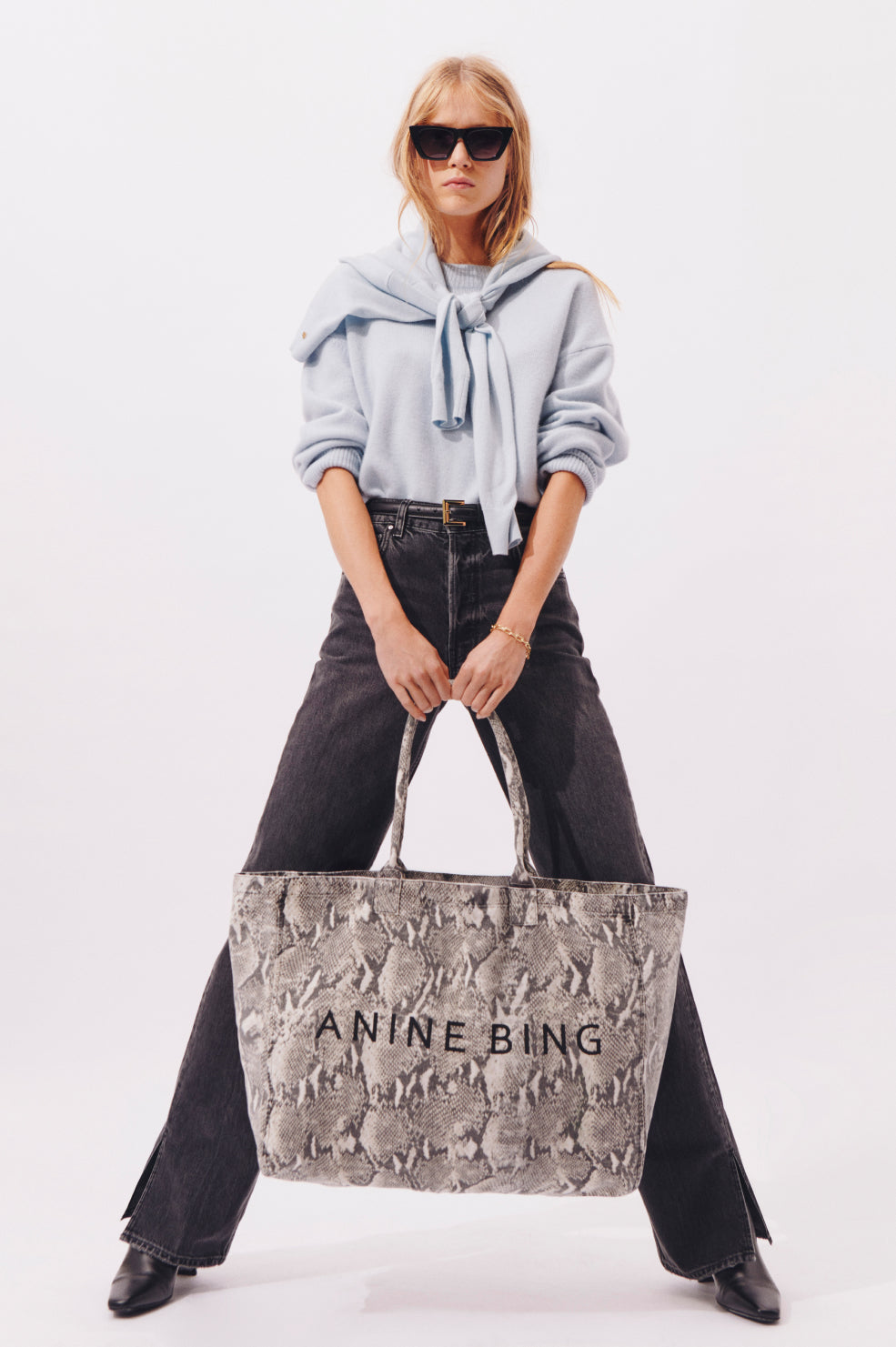 Woman holding a textured tote bag with 'ANINE BING' branding against a white background