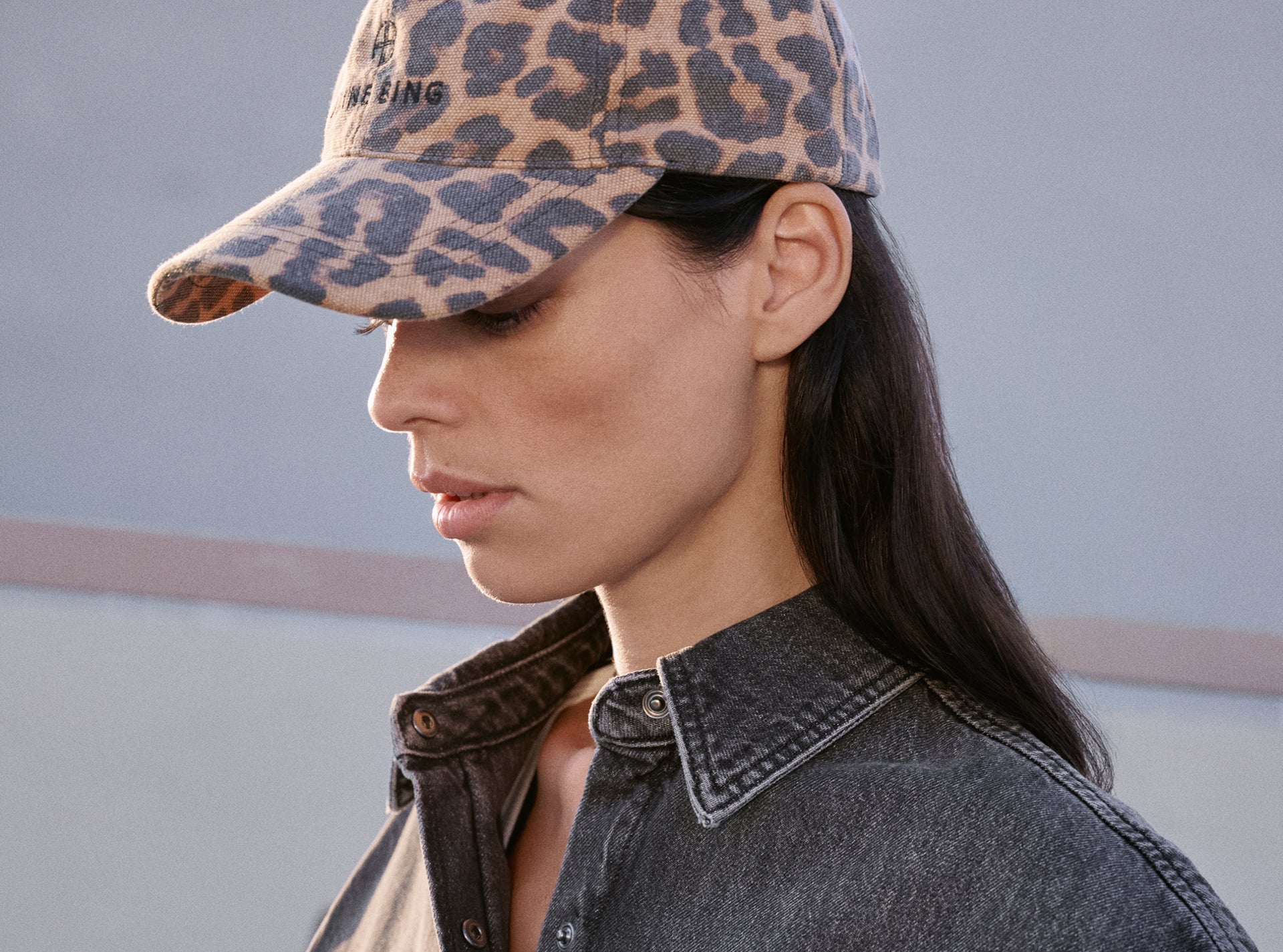 Person wearing a leopard print cap and denim jacket against a neutral background