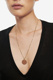 Gold chain necklace featuring a round disc charm, worn on a model with a black v-neck top.